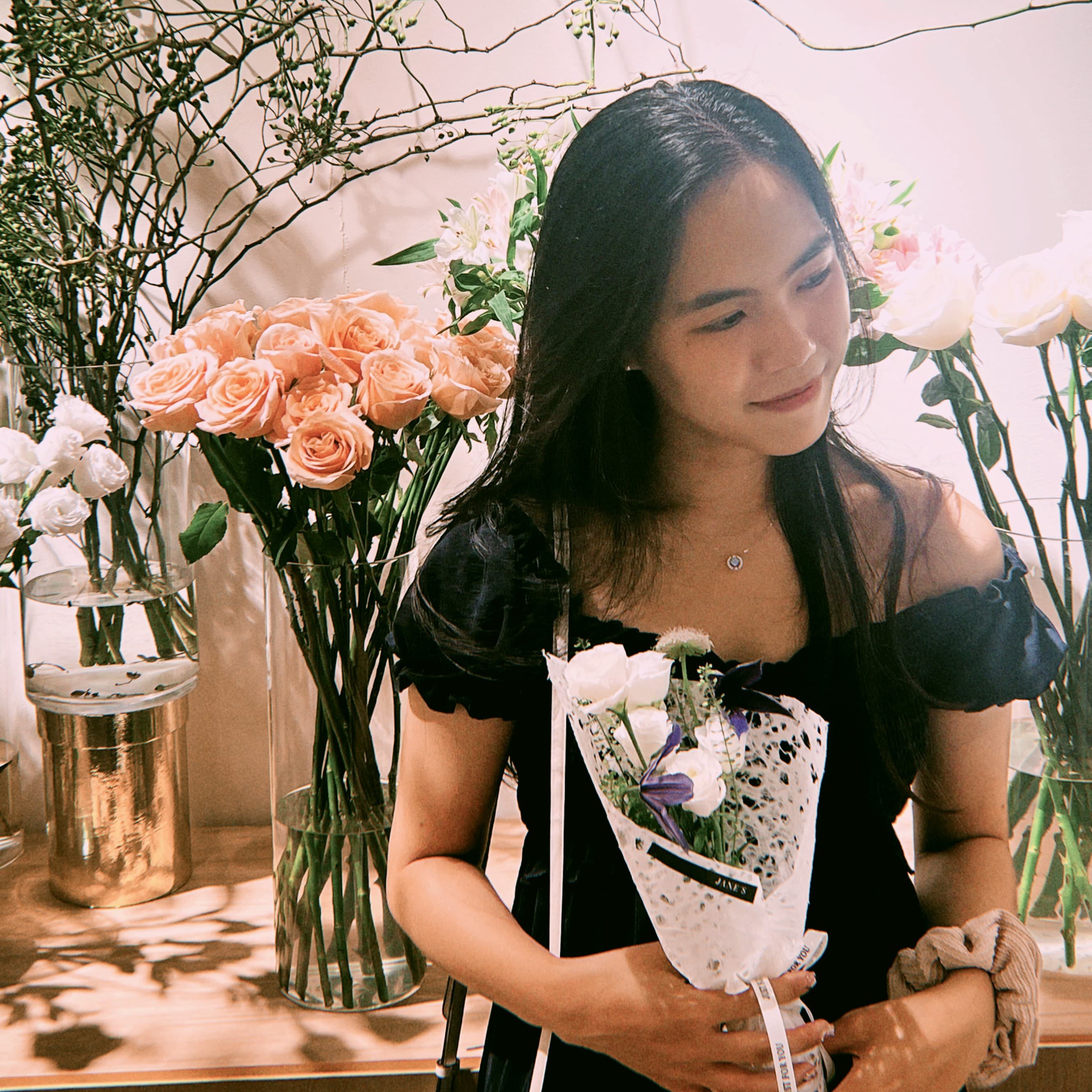 Susana holding a small wrapped flower bouquet among vases of roses