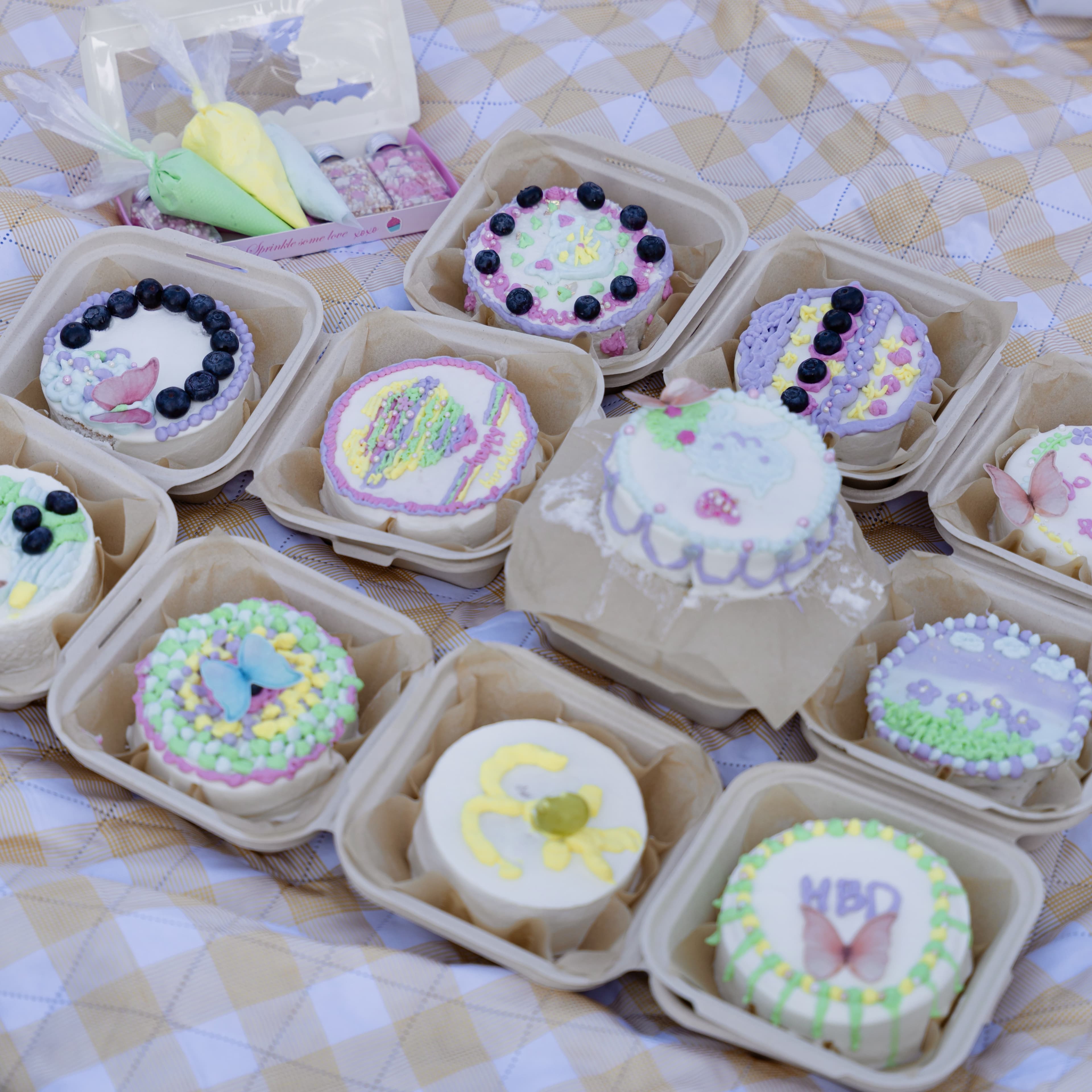 A dozen mini hand-decorated cakes in individual takeout boxes
